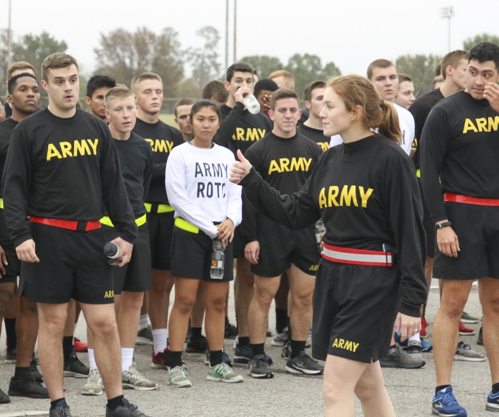 A group of people in black shirts with 'army' written on them watch a woman giving the thumbs up sign