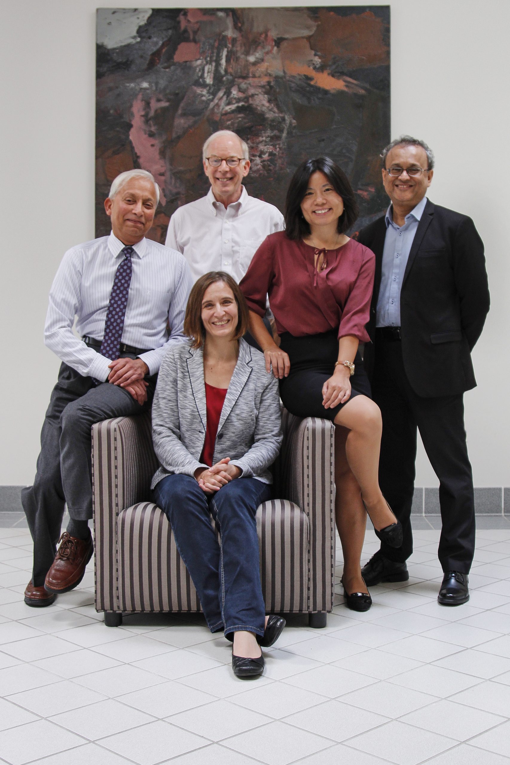 5 people pose around a chair