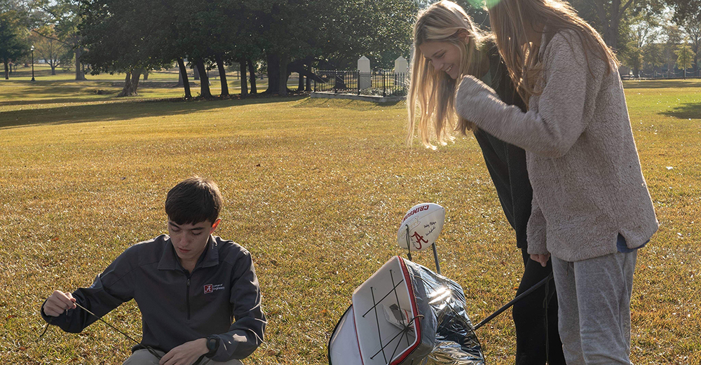 3 students outside fiddling with a project