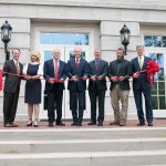 7 people cutting the ribbon in front of the new H.M. Comer