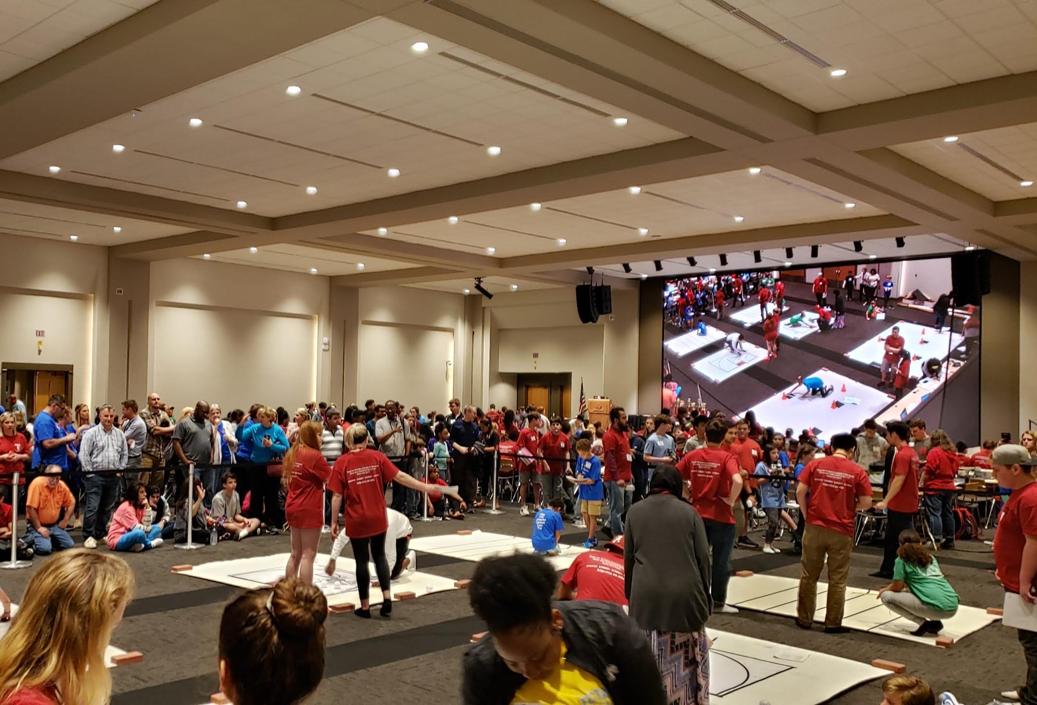 Young students work with UA students and faculty in a large room filled with people