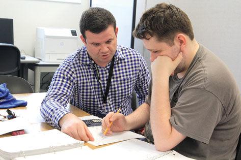 Two people work on a problem on a piece of paper at a desk
