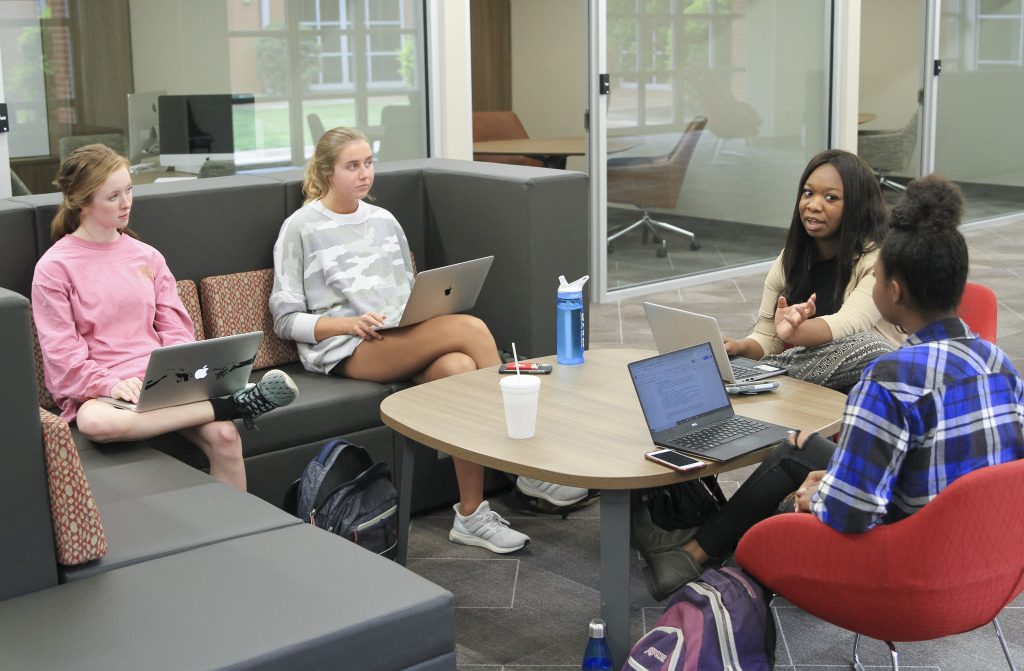 Students with laptops sit around a small table indoors
