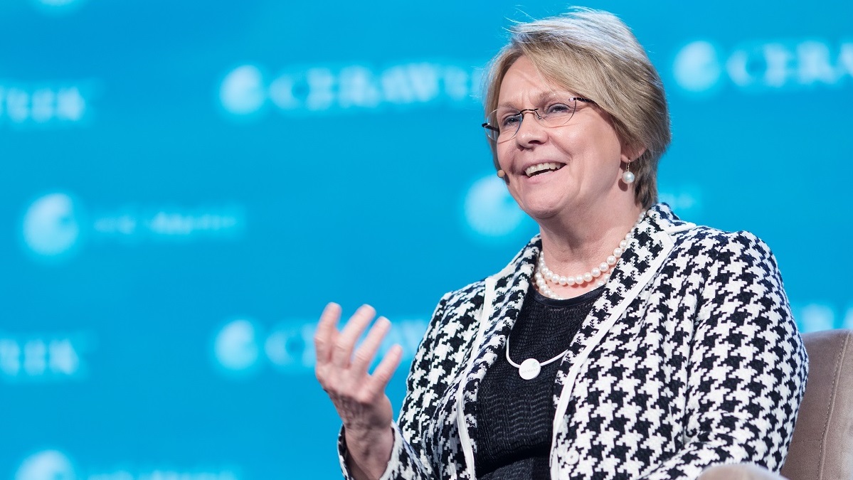 A woman in a hounds tooth jacket talks at a conference