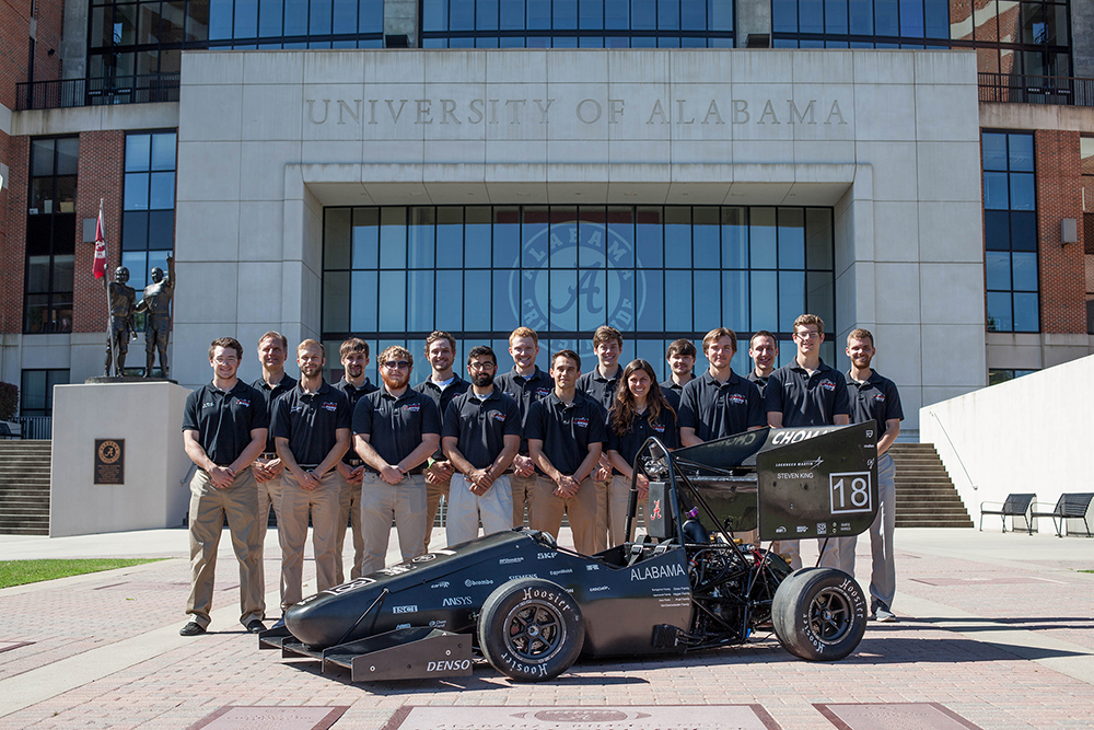 Crimson Racing team stands outside football stadium with their race car