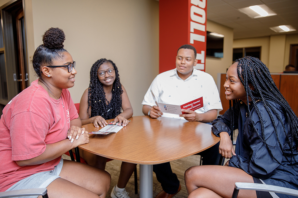 four students sit wound a table chatting