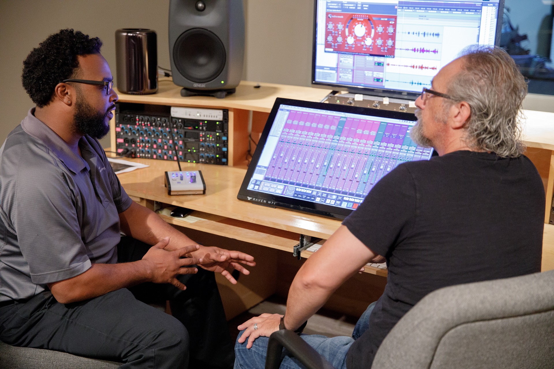 Two men talking while sitting in front of a screen showing musical levels