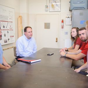 Students, faculty and alumni talk around a table in a lab.