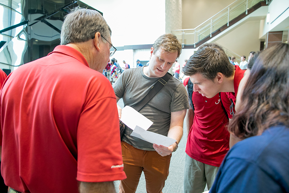 Four people look at two sheets of paper in the Ferg common area