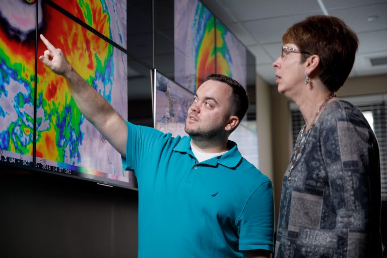 Two people looking at a hurricane model on screens