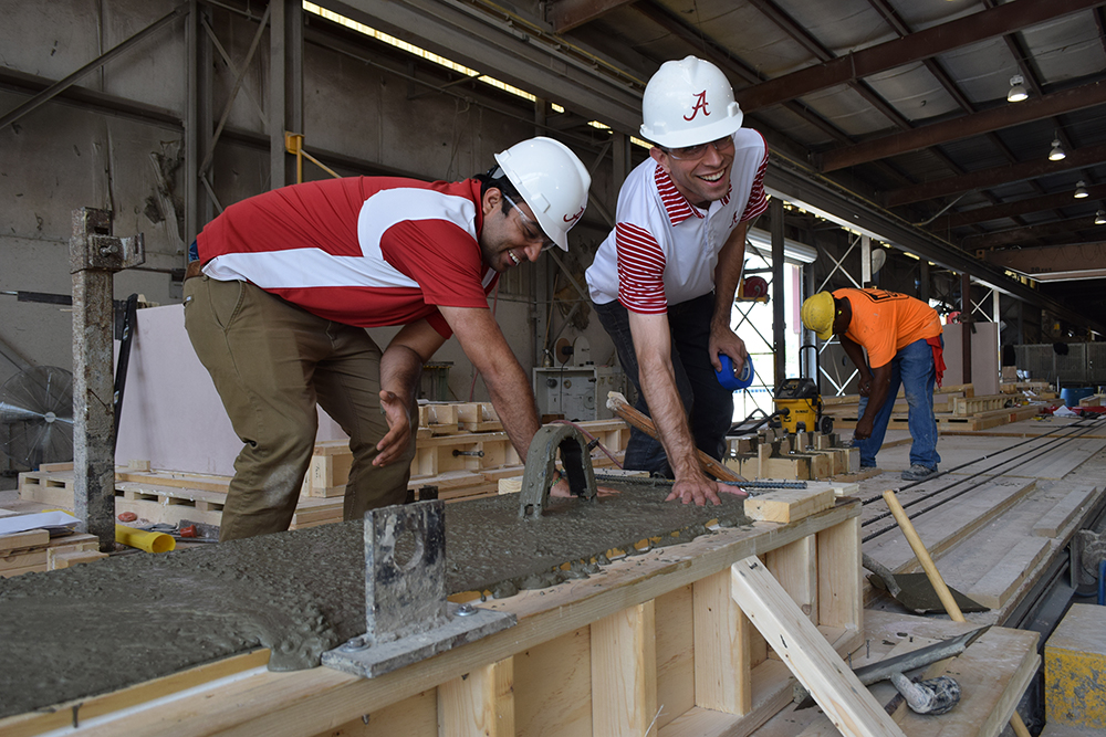 Two UA students touch a cement beam being made in a workshop.