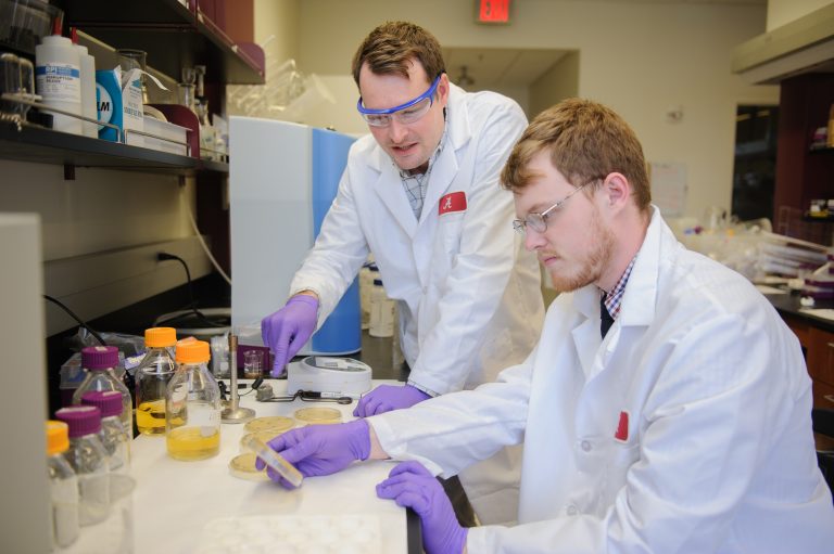 Two people in lab coats work with vials in a lab