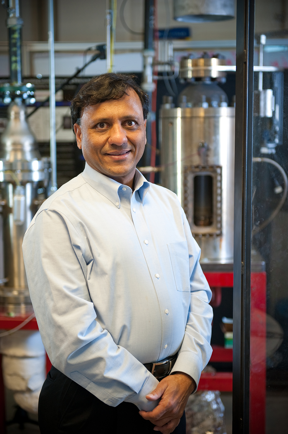 Dr. Ajay Agrawal standing in a lab with a lot of pipes in the background
