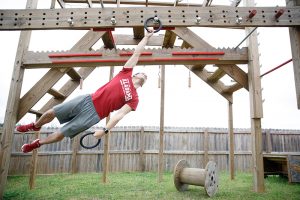 A man swings on a wooden practice obstacle course in his back yard