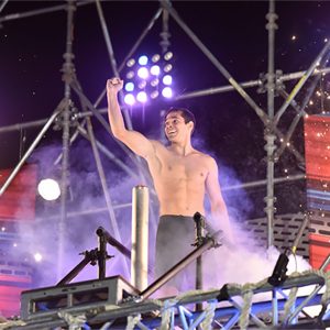 Shirtless guy stands on platform with purple lights behind him