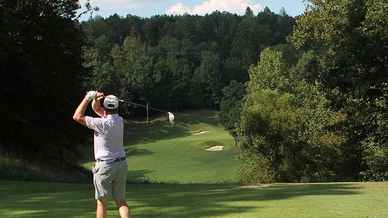 Guy on golf course completes swing towards hole