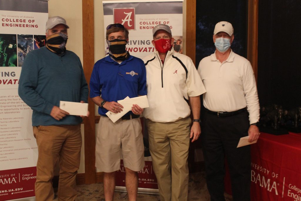 Group photo of 4 in golfing attire next to some posters about the college