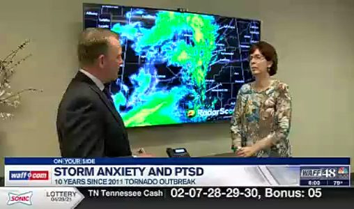 news screen capture of two people in a room with weather radar on tv