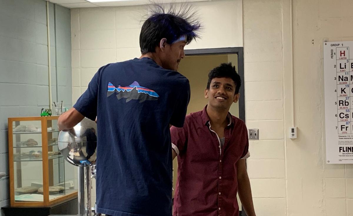 A student's hair stands on end as he touches an electric ball while another student watches