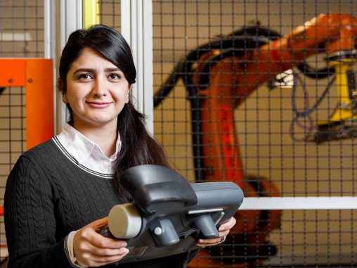 Roya Salehzadeh holds a control with a caged wielding machine in background
