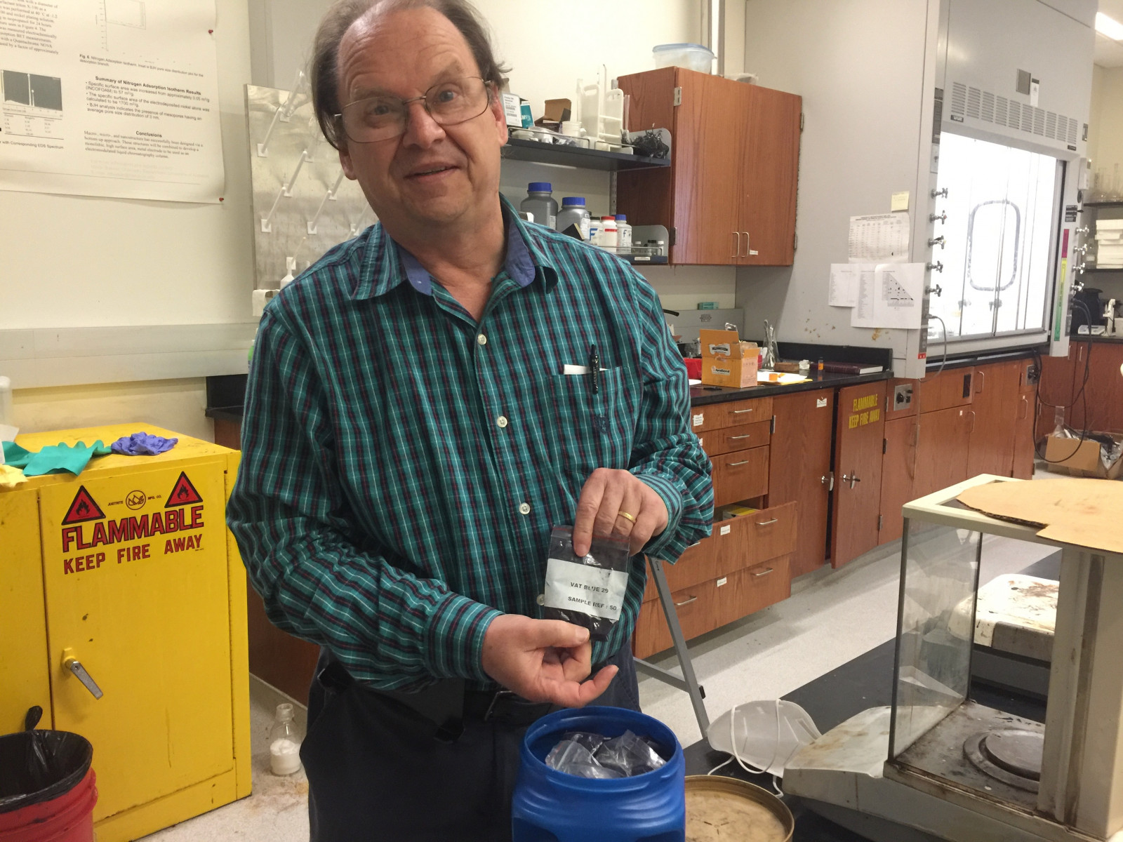 man in green patterned shirt stands in lab with shelves behind