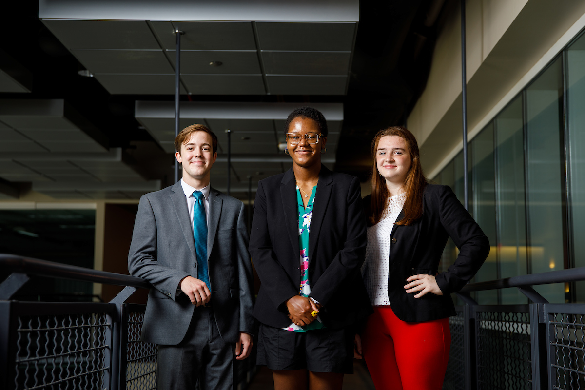 Three students in a darkish hallway with iron rails to either side