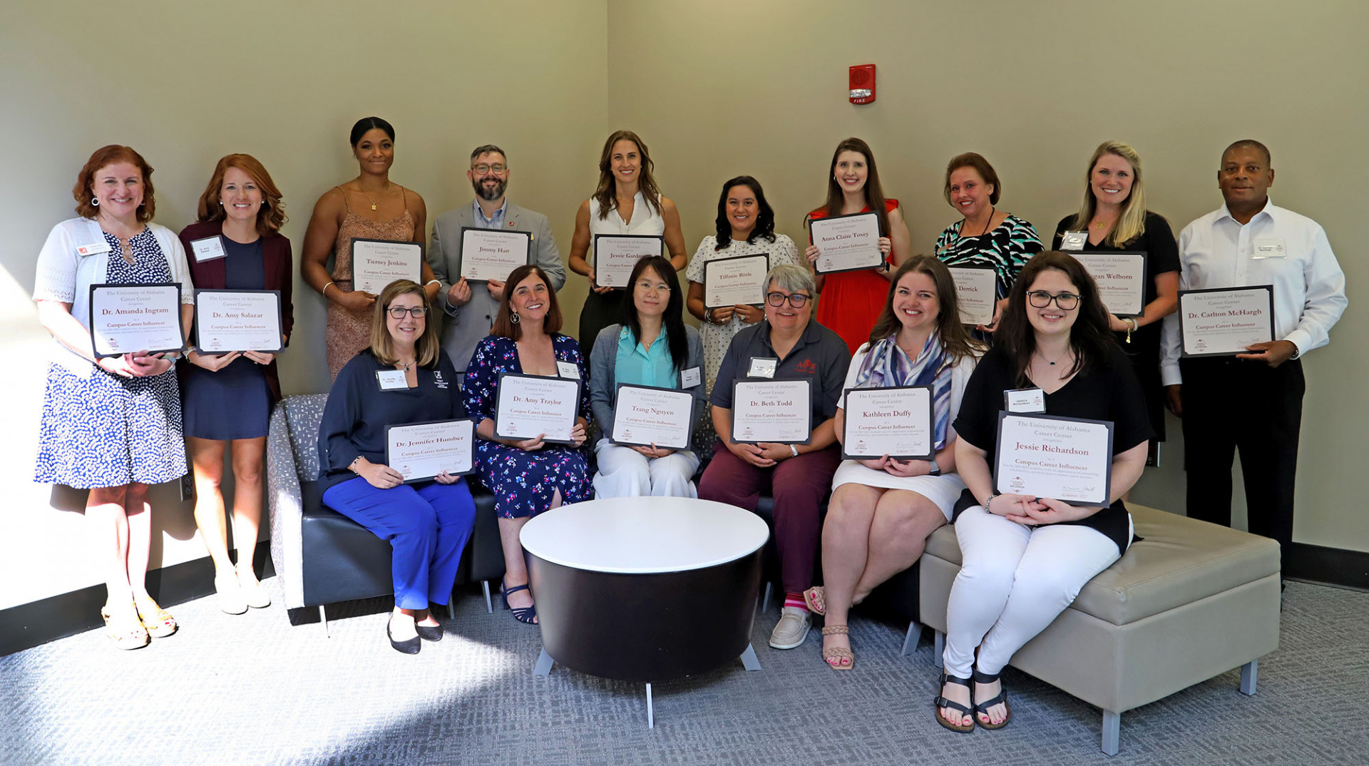 Faculty and staff stand in room holding certificates