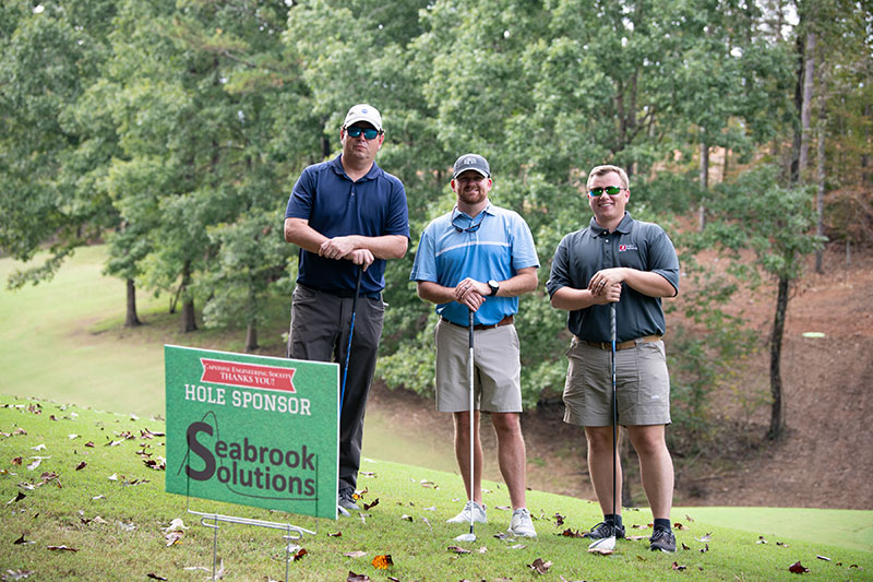3 people pose near a seabrook solutions sign