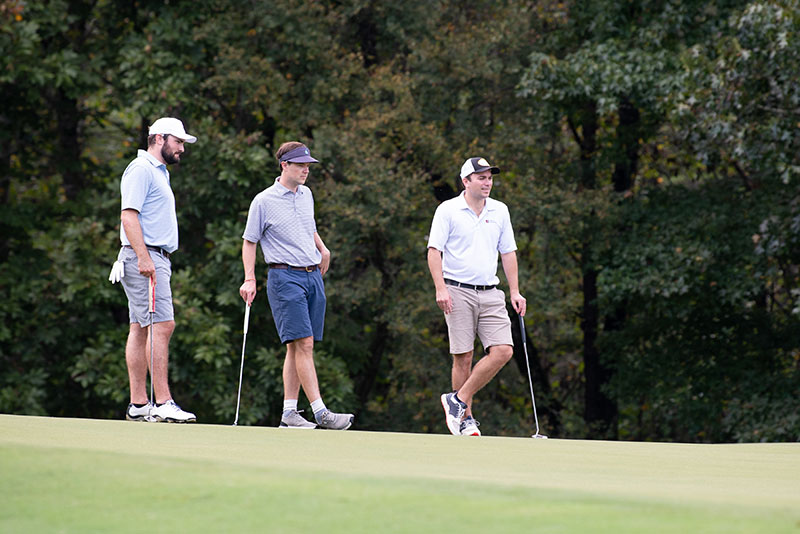 3 golfers in light colored shirts watching someone off camera