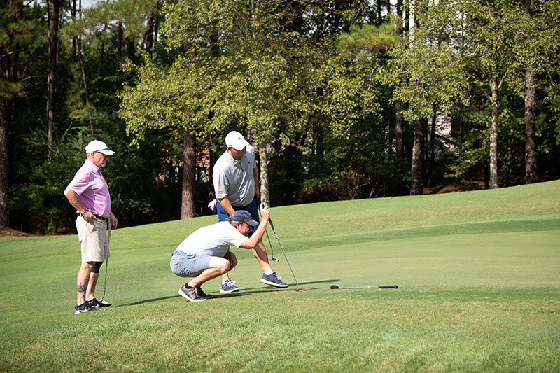 a golfer kneels on the ground while two others stand near him