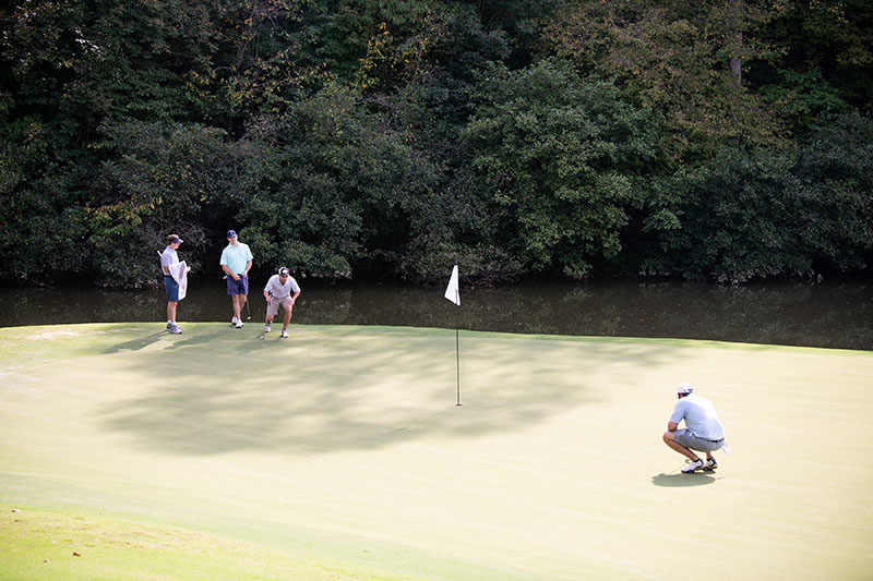 3 men on top left and one on bottom right looking over a golf hole and flag