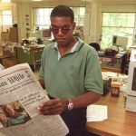 An older photo of a man in sunglasses holding a Crimson White newspaper