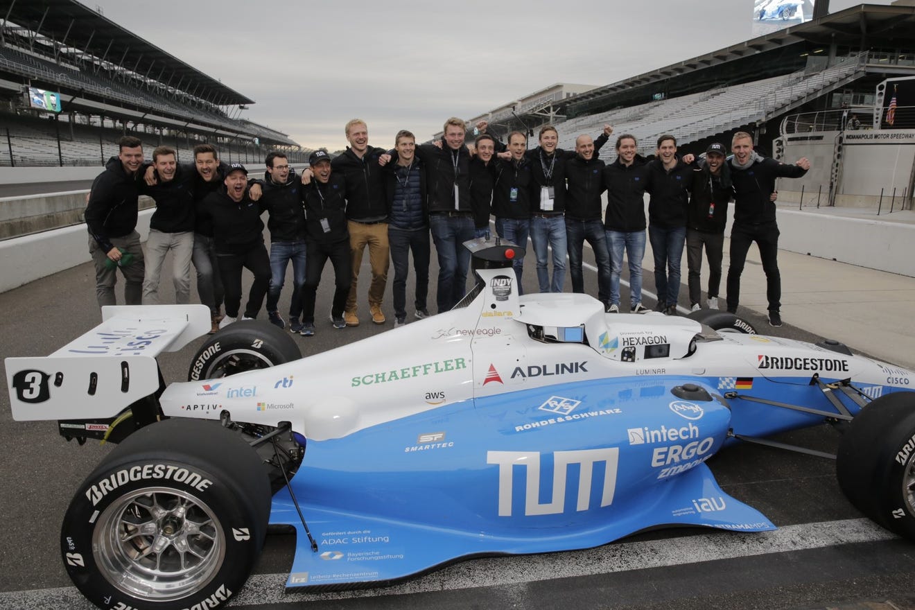 a large group of people stand behind a race car on the track