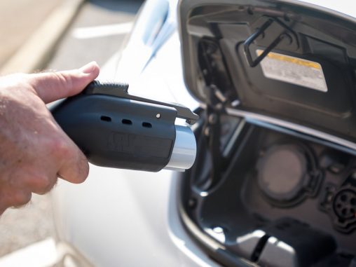 hand holding an electric car power plug next to a car