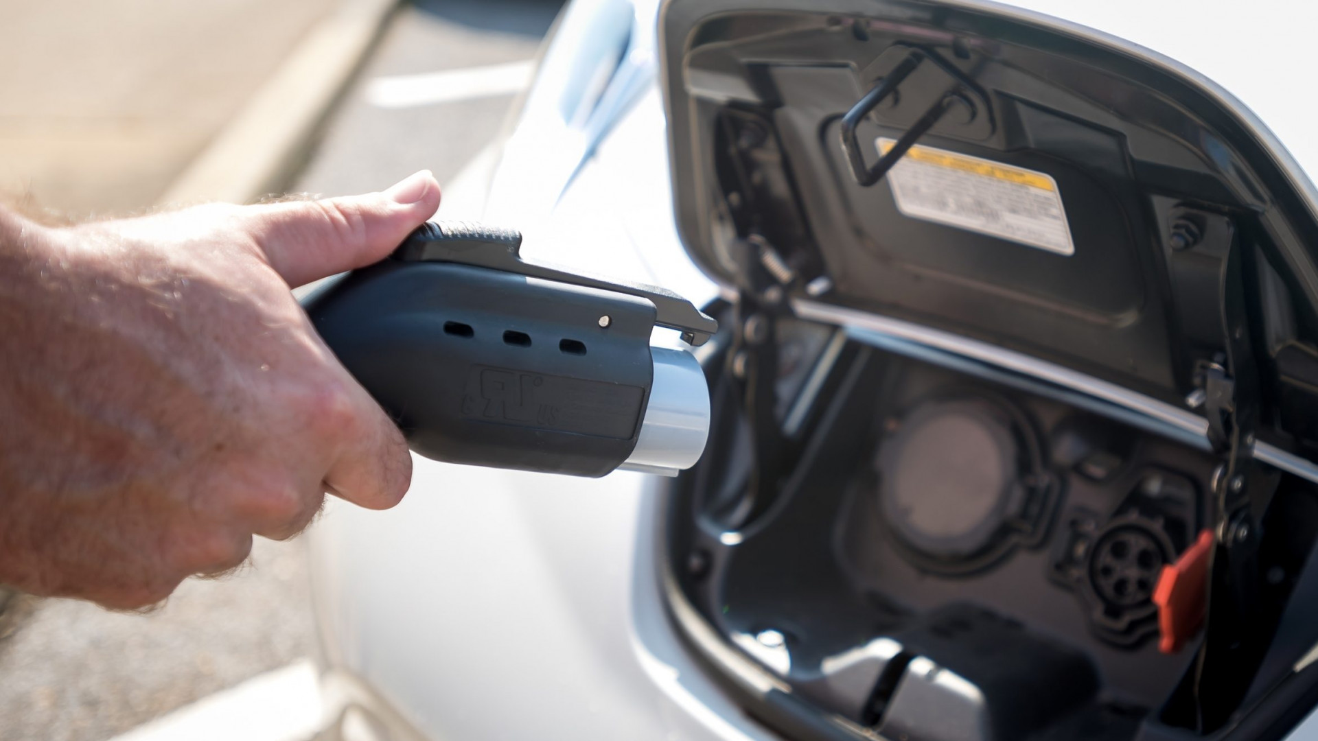 hand holding an electric car power plug next to a car