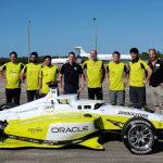 a team of people in neon yellow shirts stand behind a racecar