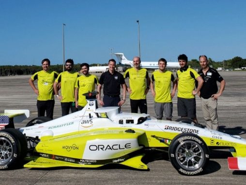 a team of people in neon yellow shirts stand behind a racecar