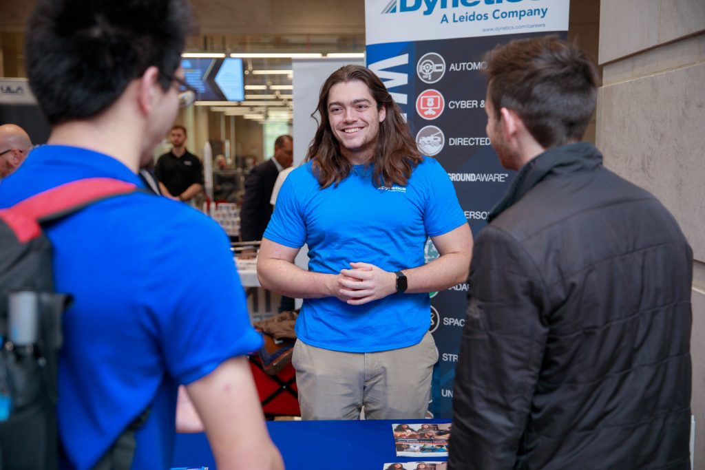 A person in a blue shirt talking to others at a booth
