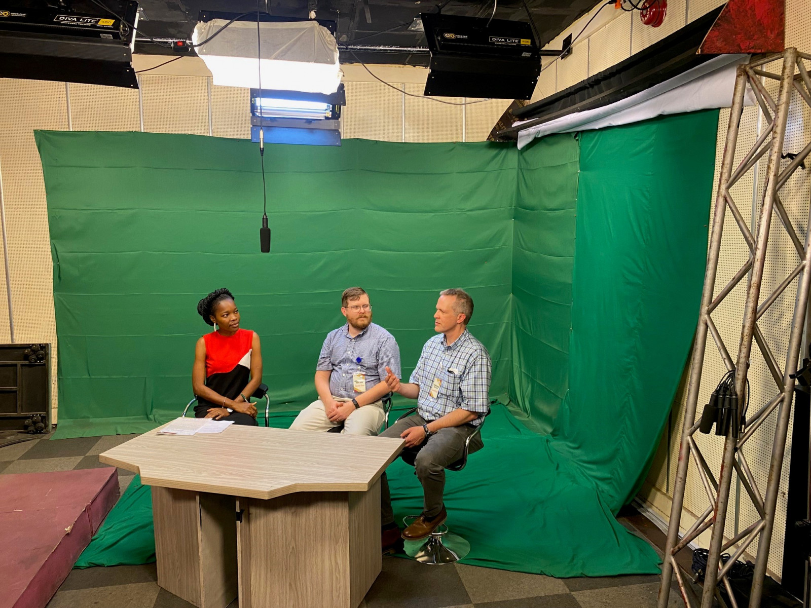 3 people at a desk in front of a green screen