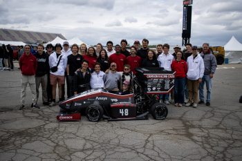a huge group stands behind a racecar