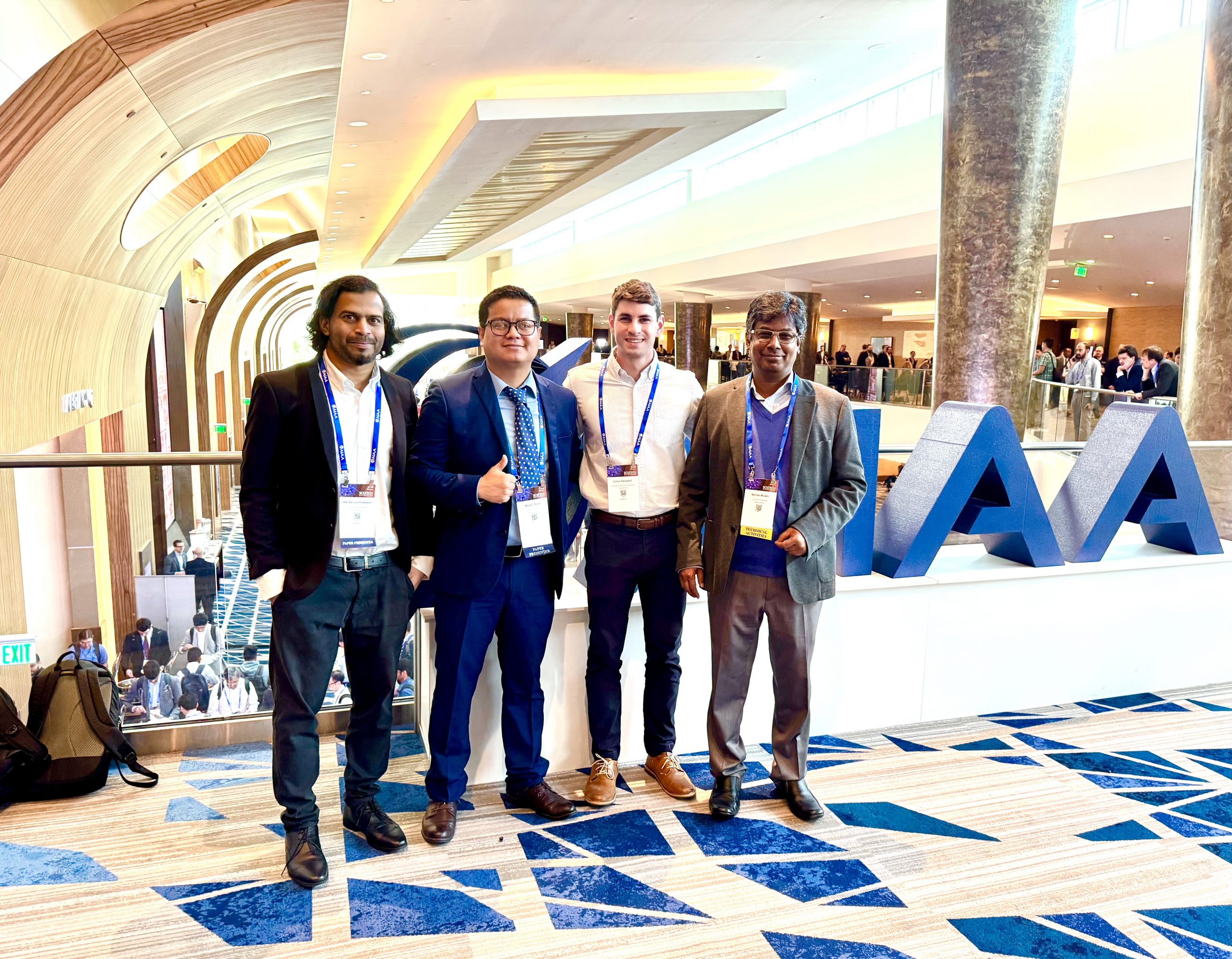 four men pose for a picture in a conference hall