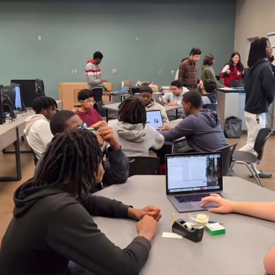 Students sit and stand collaboratively at tables in a classroom.
