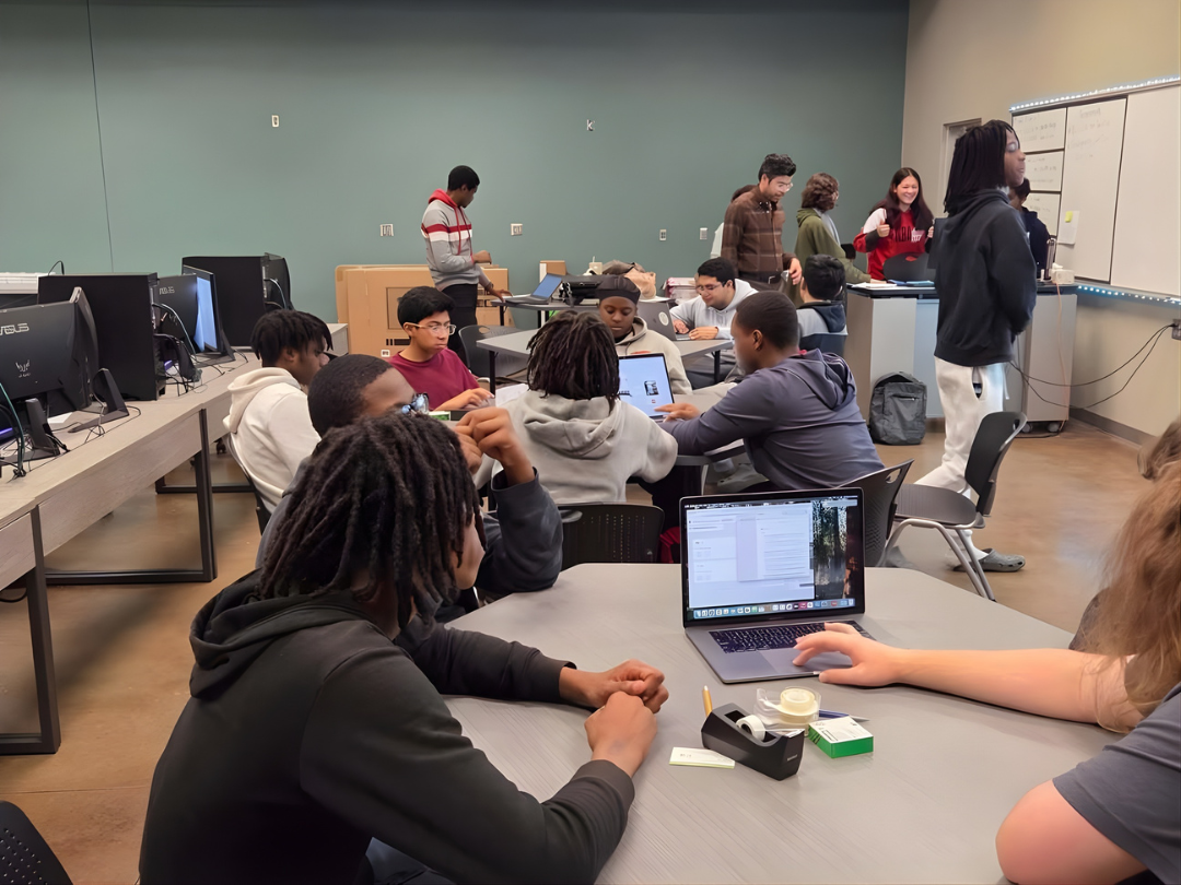Students sit and stand collaboratively at tables in a classroom.