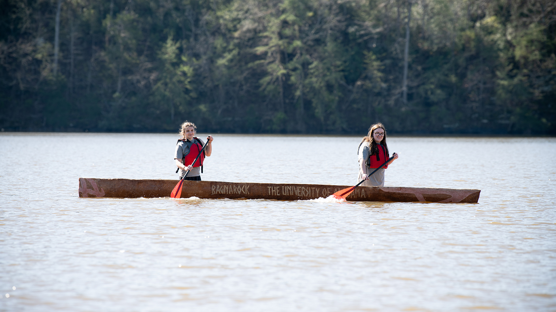 2 students with a reddish concrete canoe in the water