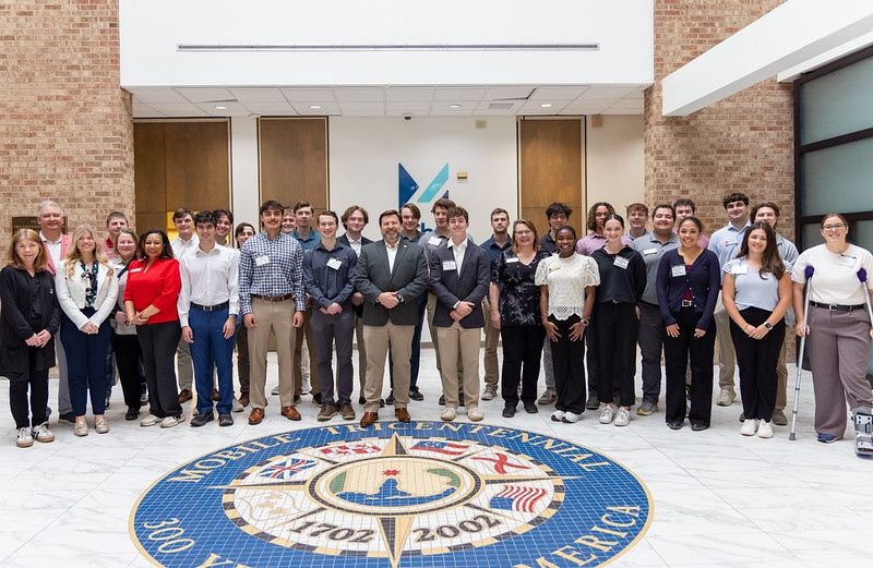 A group of students pose around the Mobile Chamber seal.