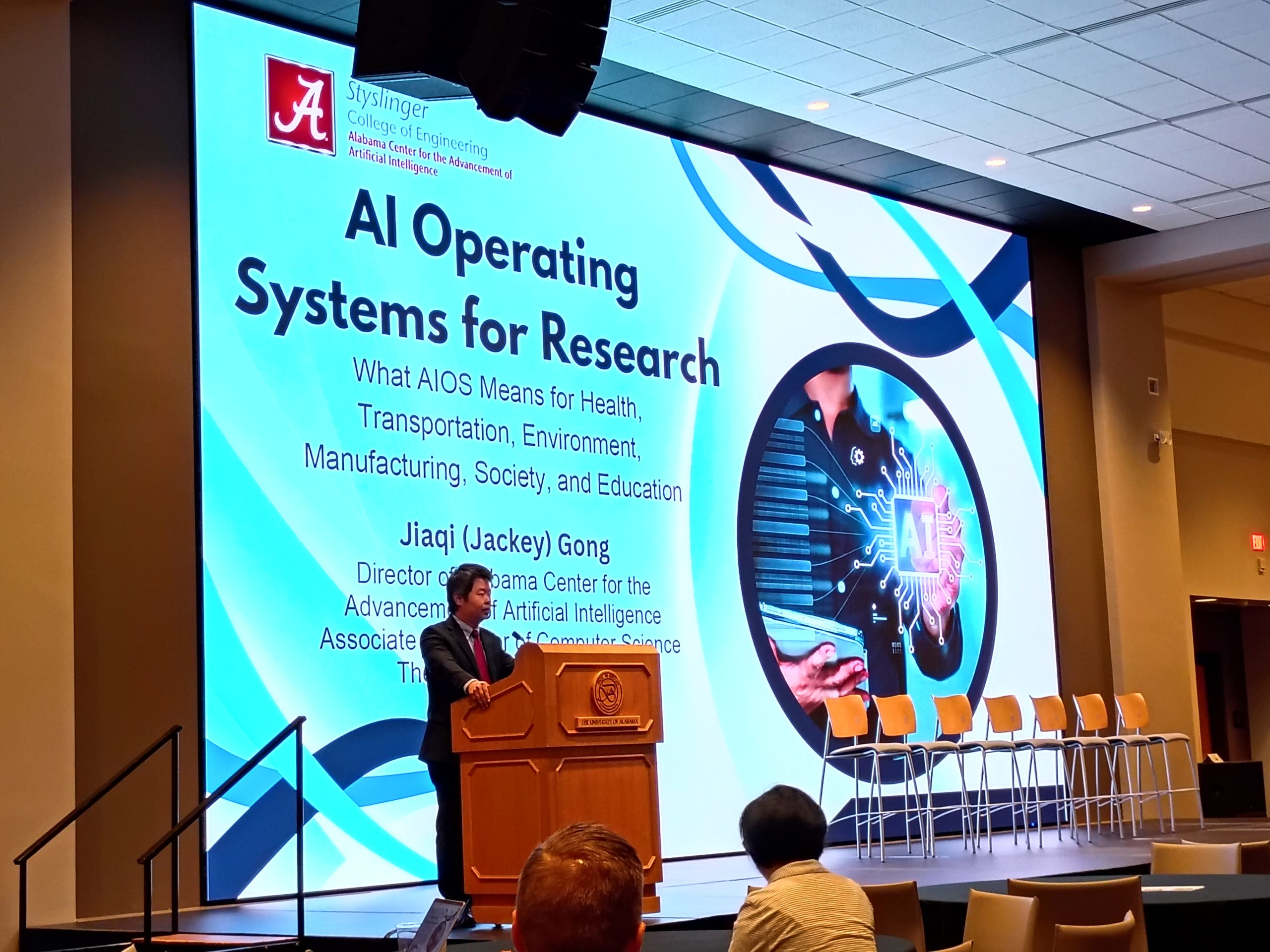 Person at a podium in front of a large screen showing a slide of research