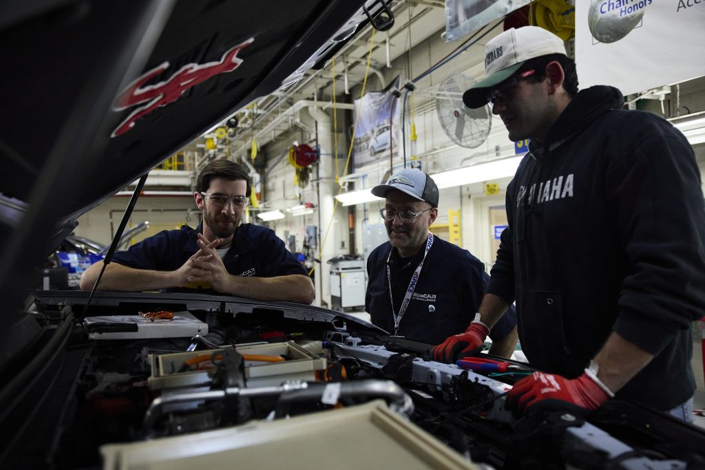 2 students and a judge looking at the car engine